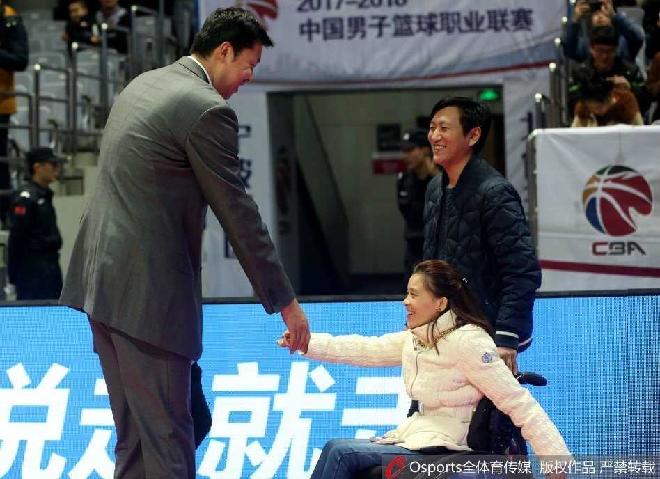 身披八一队外套的王治郅弯下腰来，目光柔和地与坐在轮椅上的桑兰交谈，他面带微笑，如同老朋友一般亲切，桑兰则抬头认真倾听，画面充满了温情。