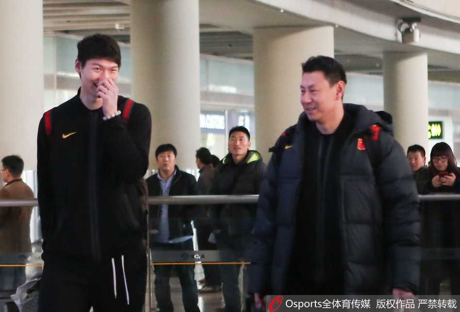 李楠指导身着国家队运动外套，面带微笑地推着行李车，眼神中透露出对弟子们的肯定与未来的期许。