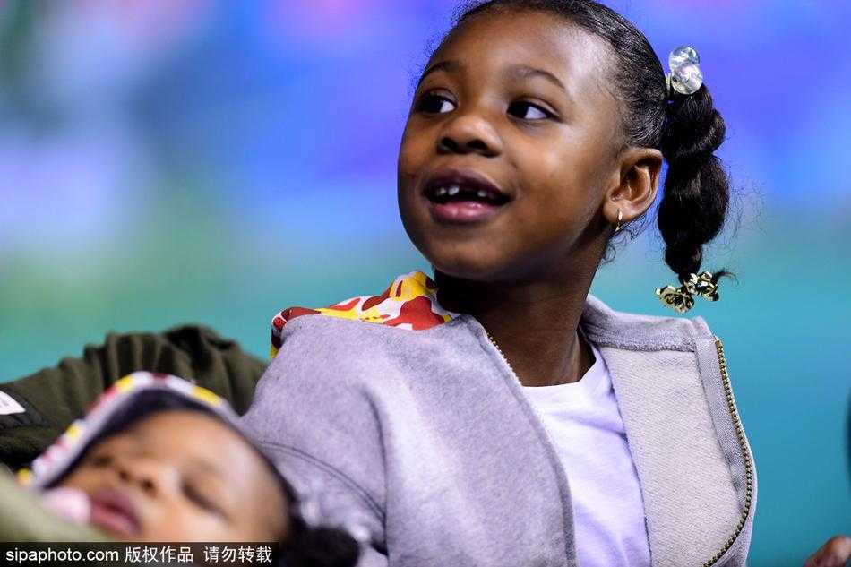 小女儿扎着可爱的丸子头，嘴里似乎含着手指，脸上带着婴儿肥，天真无邪地望着远方，仿佛在寻找爸爸巨大的身影。