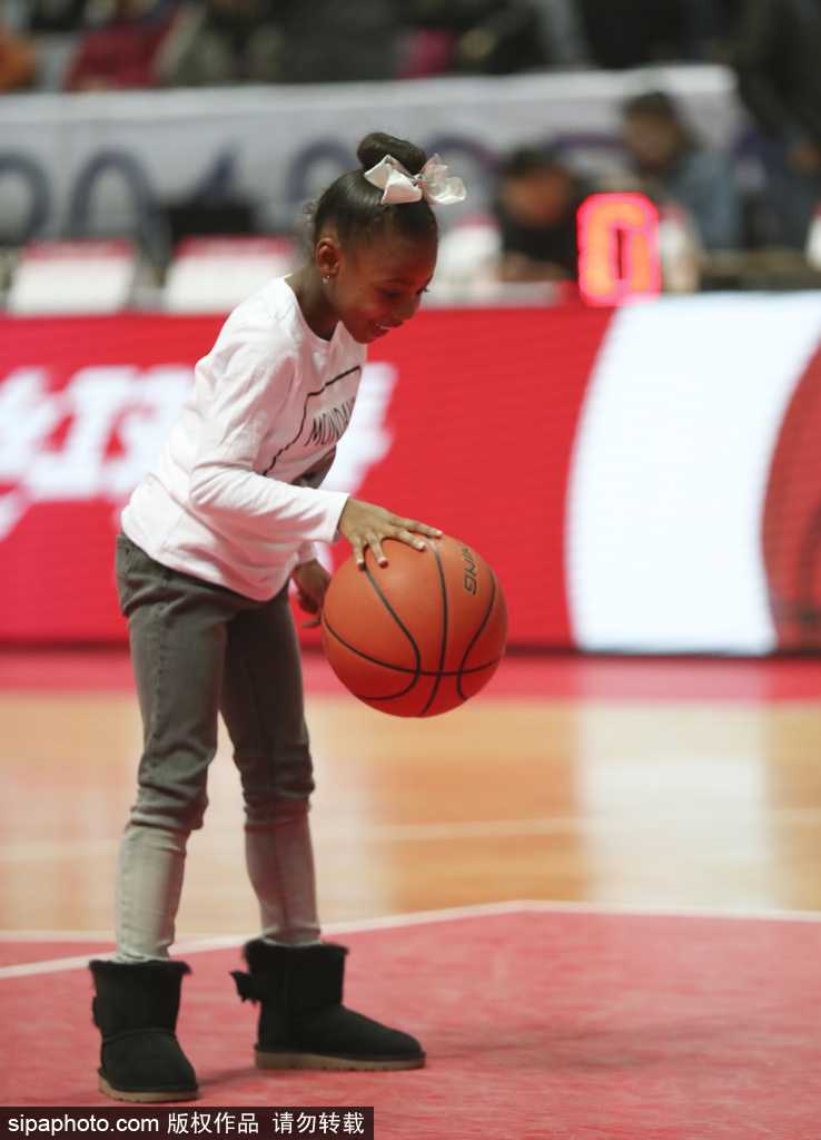 小丫头侧身对着镜头，小手用力拍打着橙色的篮球，脸蛋因为兴奋而红扑扑的，身后看台上球迷的目光都被她吸引。