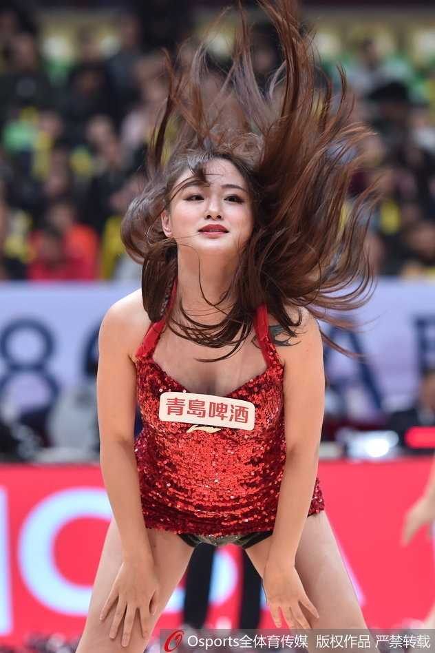 赛后篮球宝贝们在场上合影，高举手臂，庆祝又一次成功的表演，身后是退场的球迷。