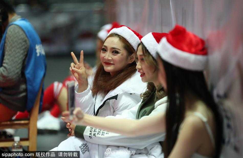 圣诞夜的雅戈尔体育馆:八一男篮背后的篮球宝贝与她们的场下瞬间 一位宝贝正在对镜整理妆容,旁边的队友拿着手机充当光线的补充板,即使在嘈杂的球场角落,她们也要保持最完美的形象面对观众。