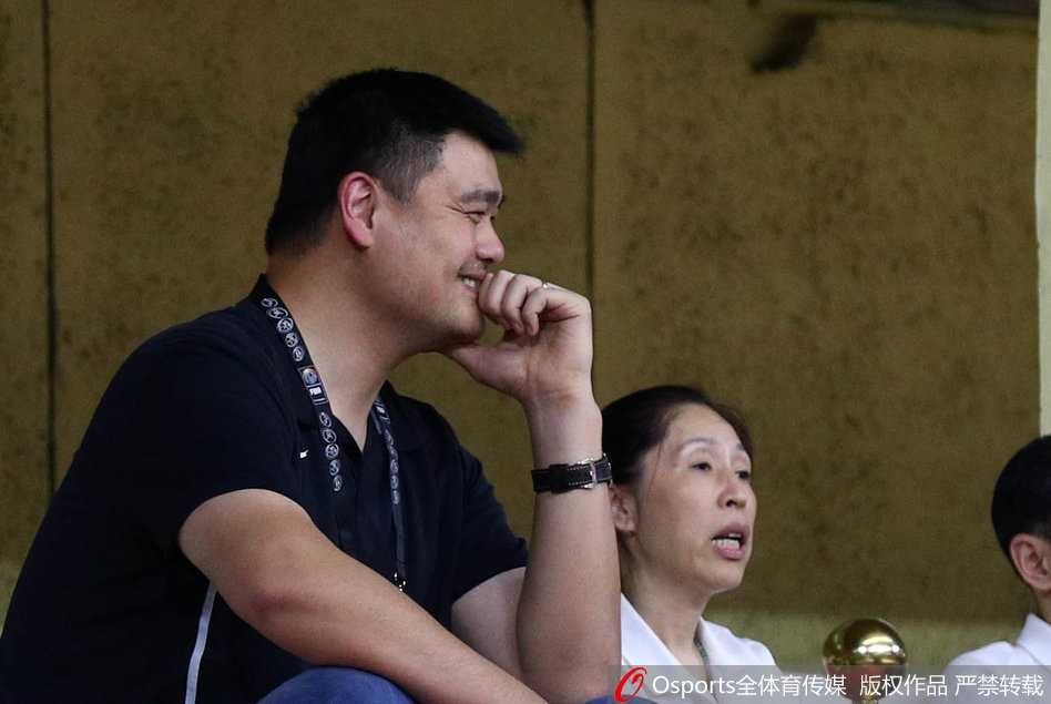 比赛临近结束，大局已定。姚明转头与身旁友人交流，他的侧脸线条硬朗，嘴角带着一丝若有若无的浅笑，眼神中透露出对这支年轻队伍未来表现的无限憧憬与坚定信念。