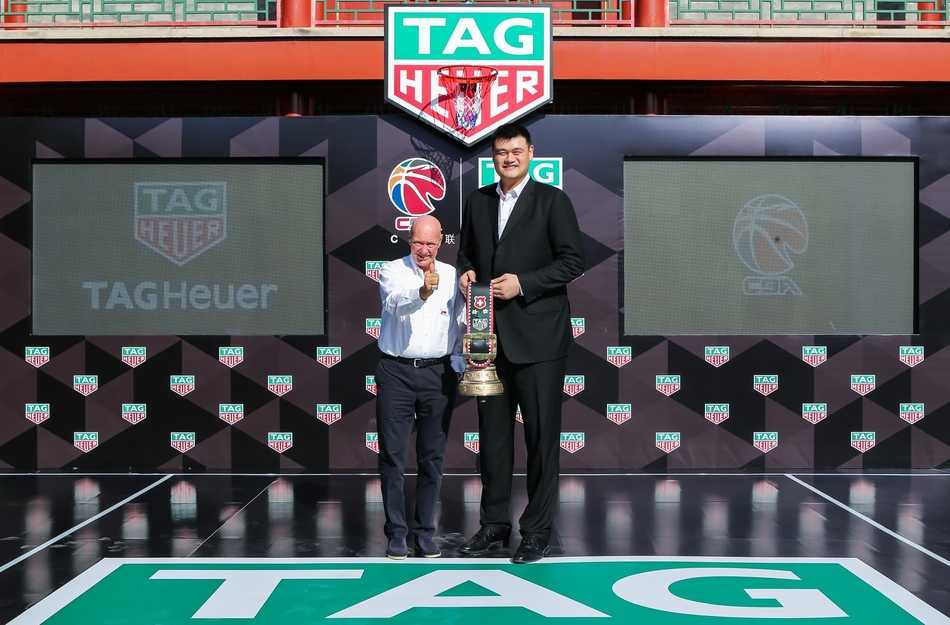 姚明携手篮球新锐 共鉴泰格豪雅重返CBA荣耀时刻 在北大朗润园万众楼前,姚明身着深色西装,面带微笑,目光坚定地注视前方,其身后是古色古香的建筑飞檐,象征着CBA传统与创新的交融。