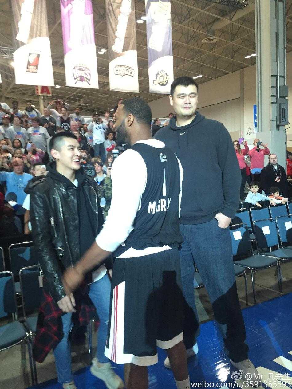 麦蒂身穿深色西装，面对镜头露出标志性的慵懒笑容，旁边的吴亦凡正专注地望向两位篮球传奇。