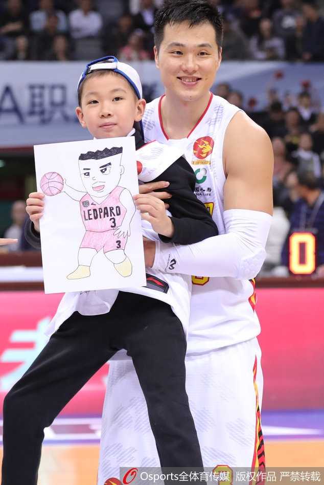 8岁的轩轩站在球场中央，略显羞涩地接过话筒，他穿着厚厚的衣服，脸上带着病容却笑得格外灿烂，身后的巨型CBA背景板衬托出他此刻成为全场焦点。