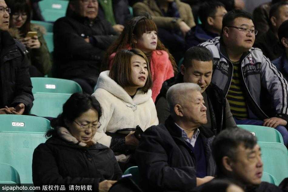 寒夜里，一位身着深色貂绒大衣的男球迷双手插兜，目光如炬地关注着场内局势，昂贵的衣装与他对篮球的专注神情相得益彰。