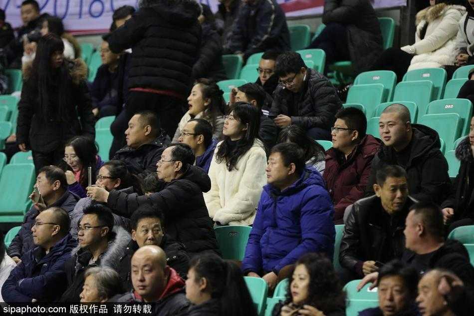 赛后，一位穿着白色貂绒大衣的女性球迷在场边自拍留念，背景是正在退场的球员和兴奋的观众，她想用这张照片记录下这个豪迈又温暖的胜利之夜。