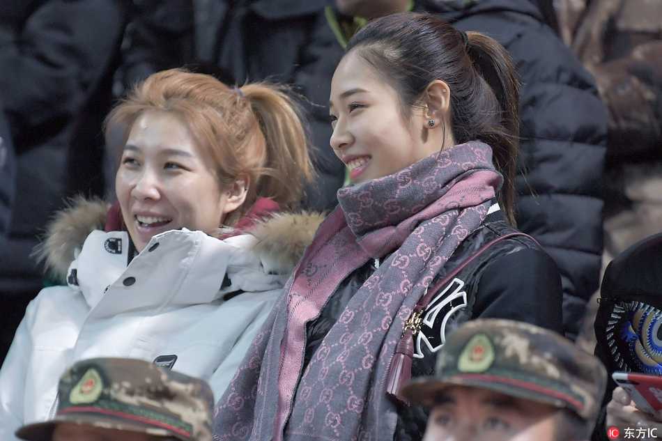 寒冬里的篮球火:吉林东北虎惜败上海,场边美女球迷惊艳长春 两位长发披肩的美女球迷并肩而坐,其中一位穿着时尚的迷彩外套,正与身旁的伙伴低声耳语,脸上洋溢着观看比赛特有的兴奋笑容。