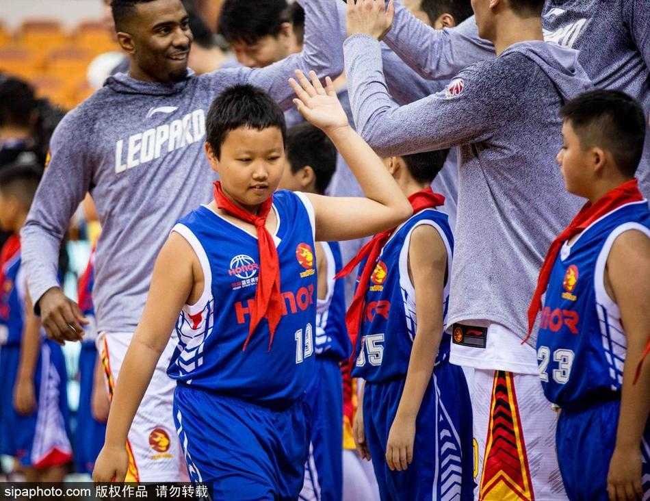 几位小小篮球迷并排而坐，聚精会神地观看比赛，其中一位孩子不自觉地模仿着场上球员的动作，小手微张，似乎正准备接下队友的传球。