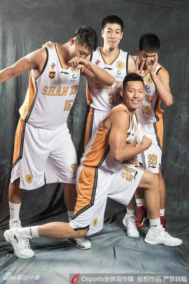 山西男篮队员在写真拍摄间隙互相搞怪打闹，一位队员正偷偷伸手拍向队友肩膀，表情狡黠，被抓拍的瞬间充满了欢乐的气氛。