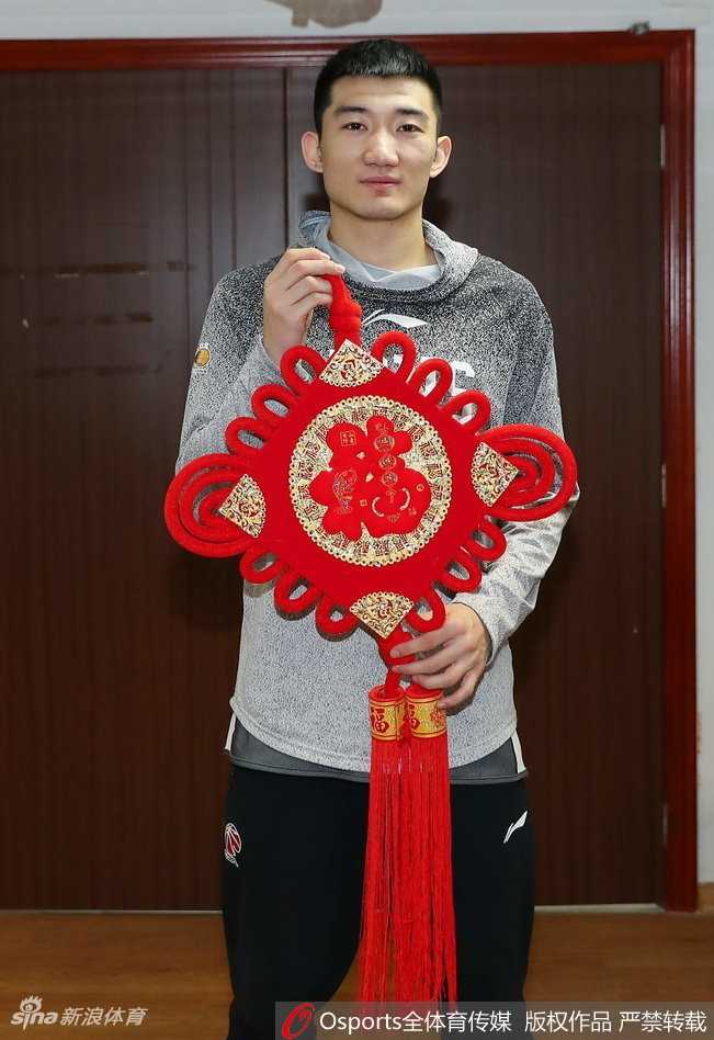 年轻球员展示春联时目光坚定，红色的纸张映衬着他青春的脸庞，寓意着广厦队的未来红红火火，充满希望。