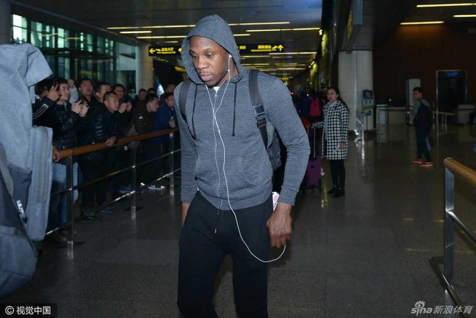 哈德森戴着黑色毛线帽和红色耳机，身背双肩包，双手插兜，面无表情地低头匆匆穿过人群，仿佛将自己封闭在独立的世界里，隔绝了周围的嘈杂。