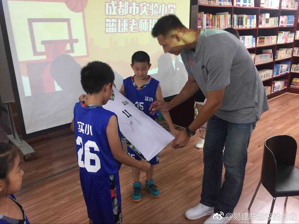 身高近2米13的易建联穿着休闲装站在成都实验小学的校园里，他正低头认真观看小学生们创作的熊猫主题画作，脸上露出温暖的笑容，与身旁活泼可爱的孩子们形成最萌身高差。