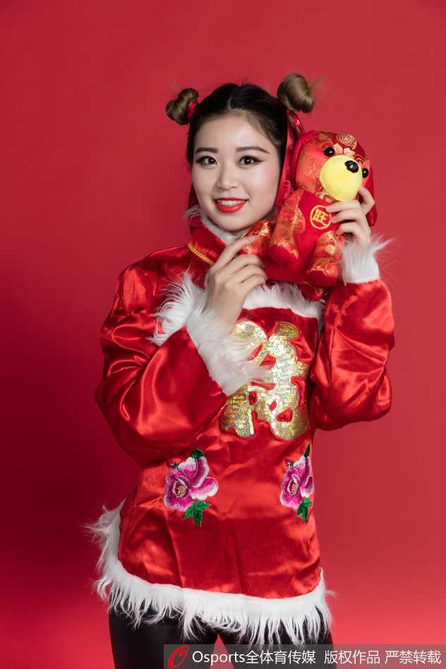 宝贝轻抚发髻，一身明艳民俗装束在红色背景衬托下更显喜庆，眉眼间流露的娇俏与温柔，恰似新春最美好的祝福。