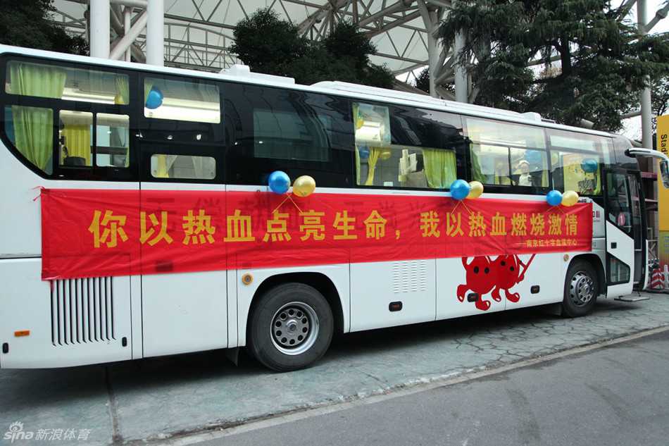 一辆喷绘着爱心标志的南京红十字血液中心献血车静静停靠在五台山体育馆外，车身标语在夜色中格外醒目，邀请过往球迷为生命加油。