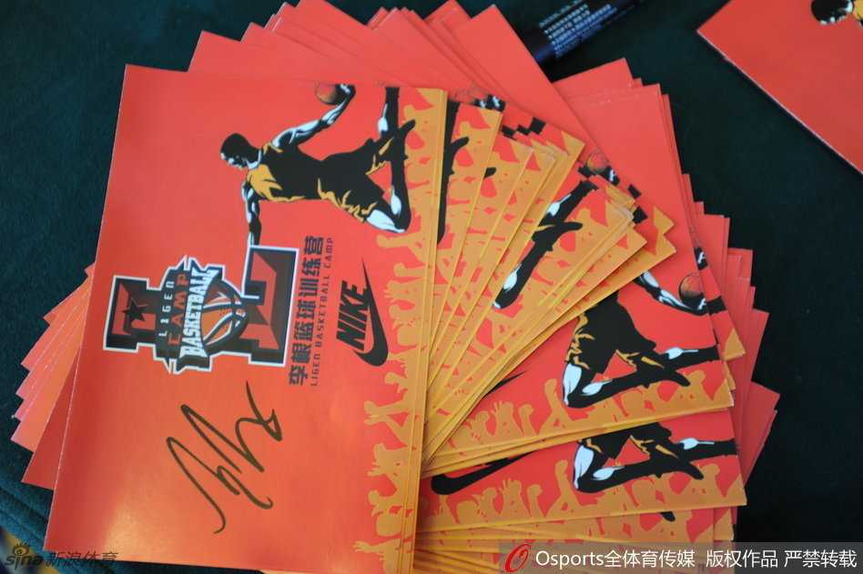 李根俯身接过孩子们递来的明信片，嘴角上扬露出标志性的憨厚笑容，眼神里满是惊喜与宠溺，仿佛看到了儿时那个追着大哥哥索要签名的自己。