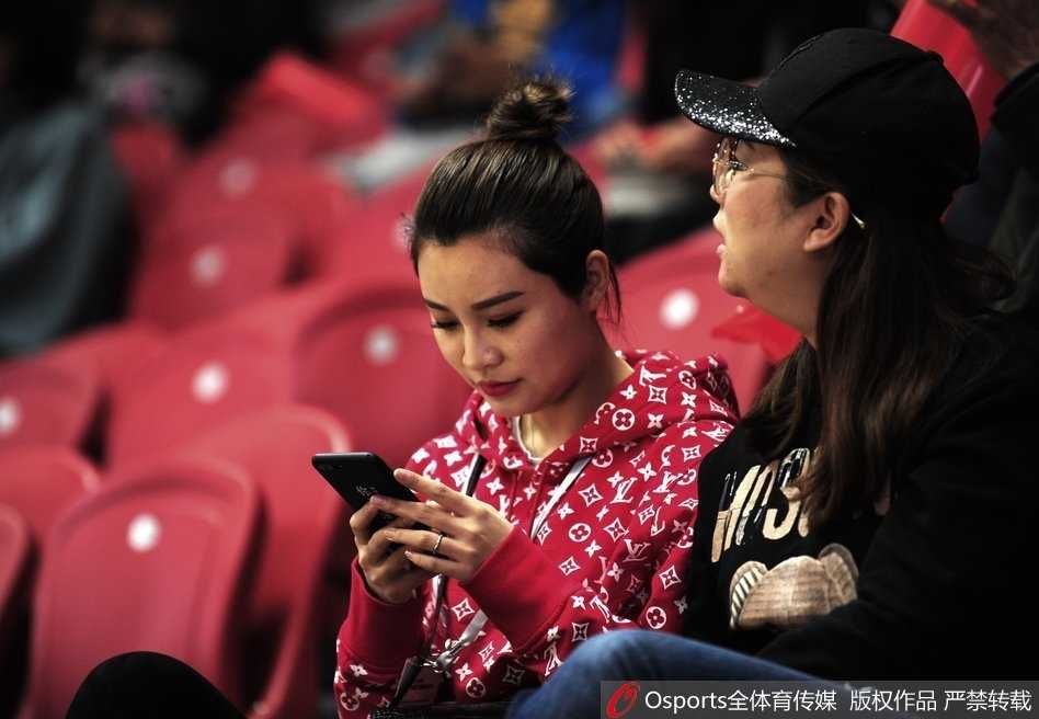 看台上的李根妻子与友人热聊，她时而掩面微笑，时而紧张凝视球场，表情随着比赛的跌宕起伏而变化，内心牵挂可见一斑。