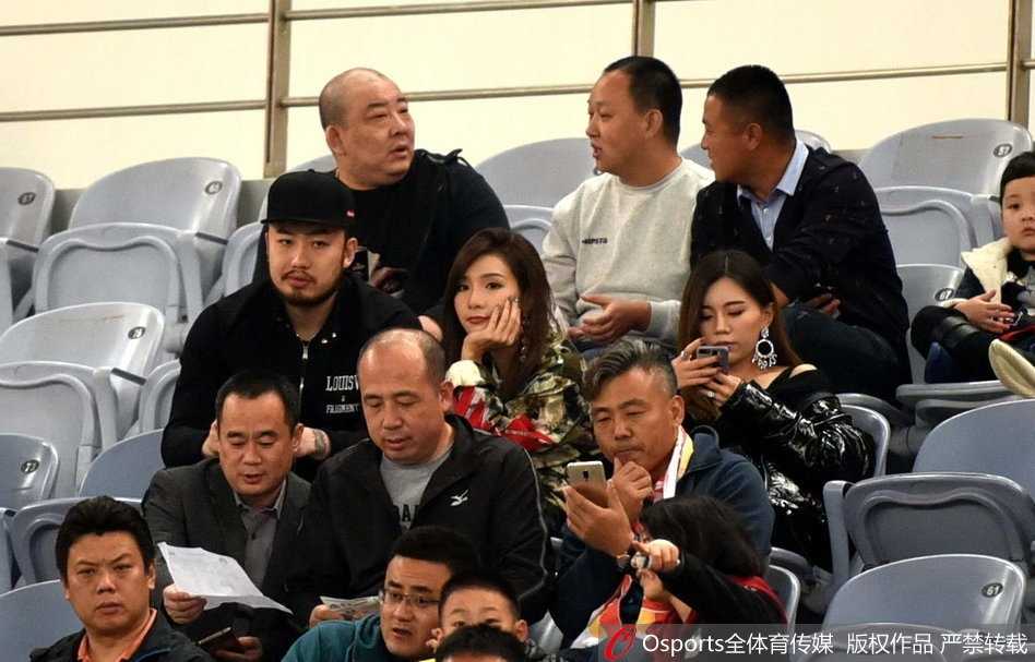 睢冉侧身指向场内，似乎在为妻子讲解着足球战术，妻子则专注凝视，脸上挂着甜蜜而温柔的笑容。