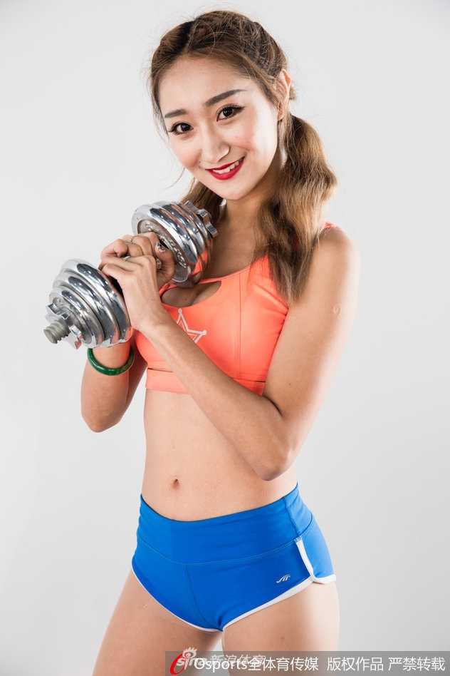 宝贝侧身坐在健身椅上回眸凝视镜头，手持哑铃的手臂线条流畅有力，运动背心下摆露出迷人的马甲线痕迹