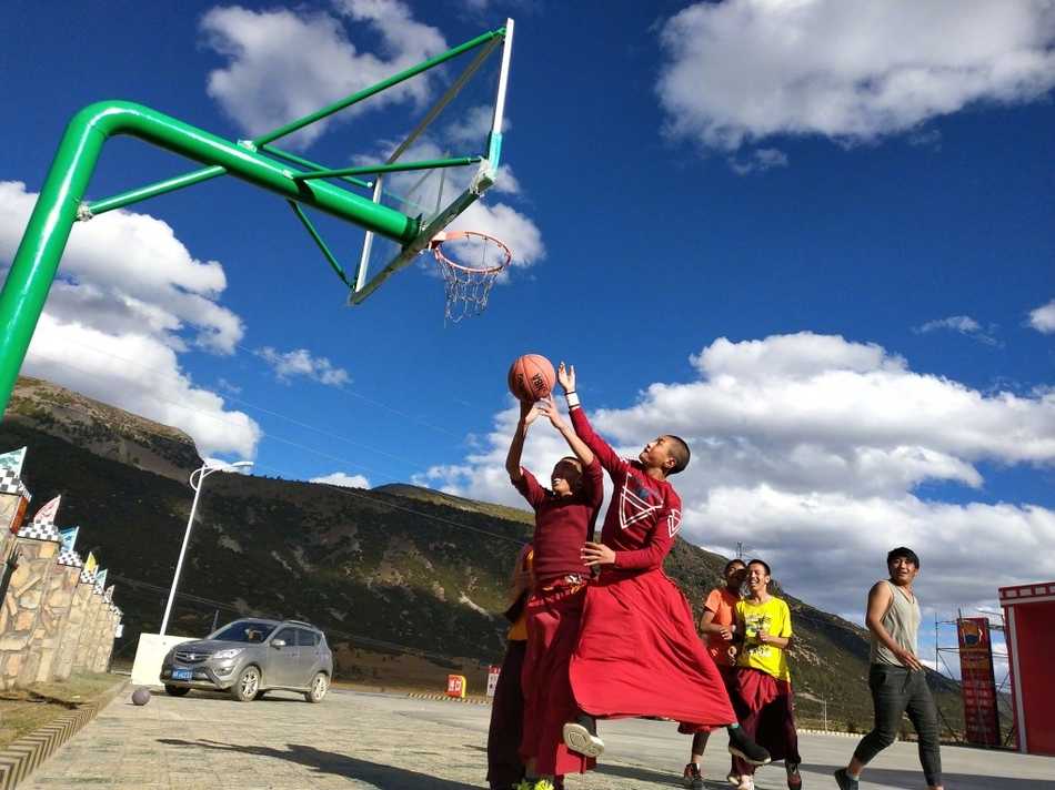 在高原湛蓝的天空下，一位身着绛红僧袍的喇嘛高高跃起，手中的篮球仿佛要挣脱地心引力，他的身影在简陋的篮球架前显得格外轻盈而专注。