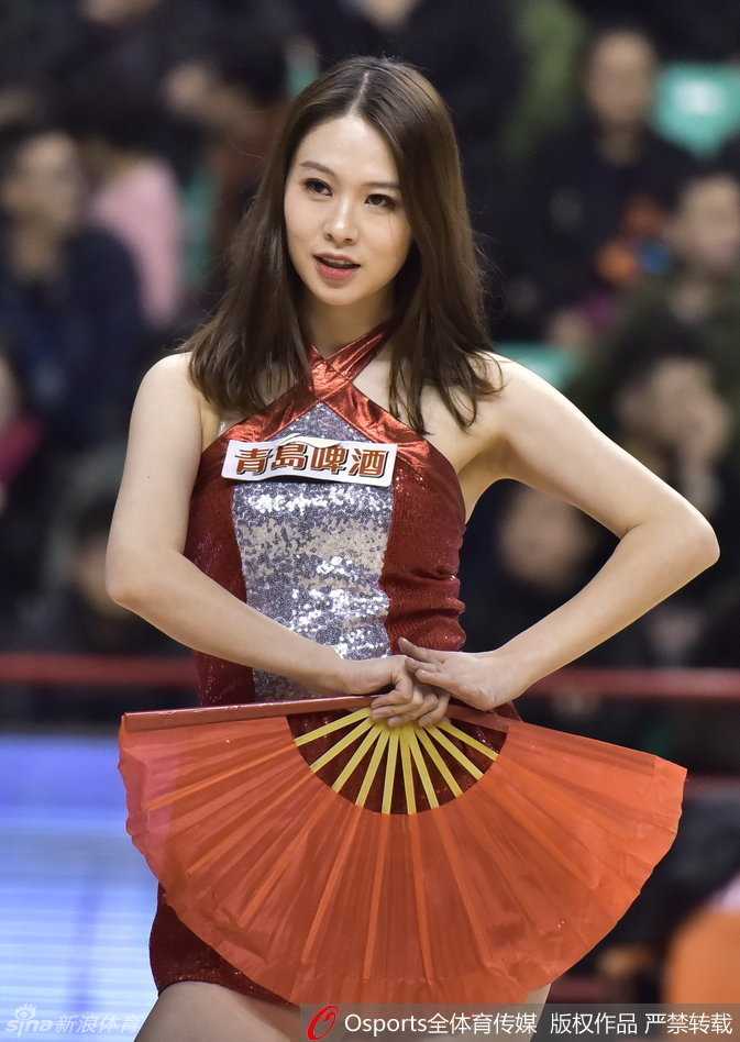 红扇摇曳燃赛场,篮球宝贝演绎青春热舞风情 赛场灯光下,一位篮球宝贝自信地甩动秀发,眼神坚定地目视前方,背后的巨大篮球海报映衬出她此刻的主角光环。