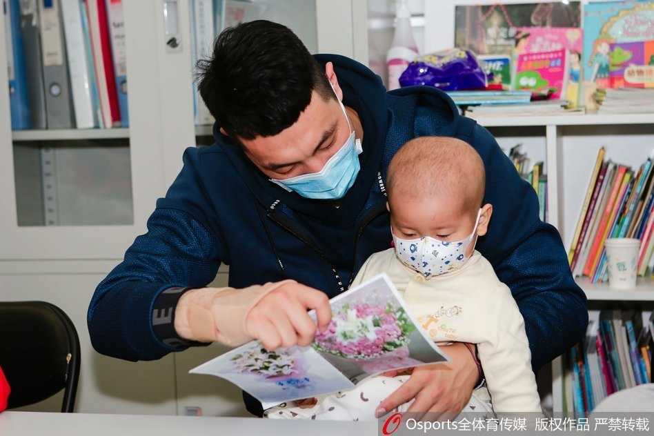 张松涛弯腰将一个大号的霹雳鸭玩偶递给坐在病床上的小朋友，小朋友双手伸出准备接过礼物，眼睛里闪烁着惊喜与兴奋的光芒，旁边病床上的家长也露出了欣慰的笑容