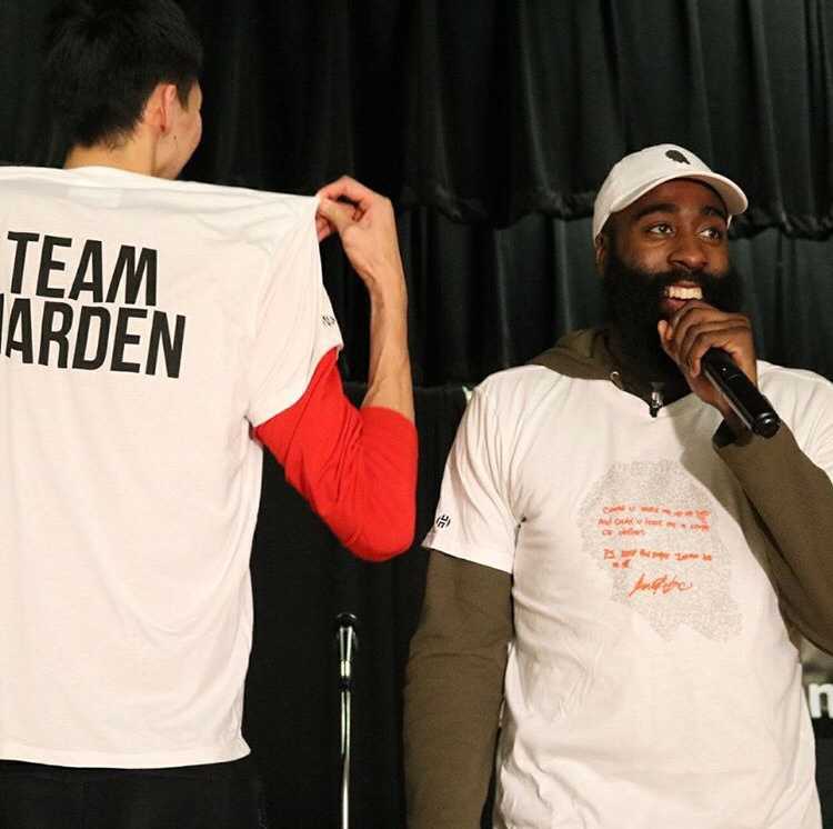 周琦身穿灰色T恤，在哈登与阿里扎的注视下，专注地手持餐勺为市民盛菜，脸上洋溢着略带羞涩的笑容。