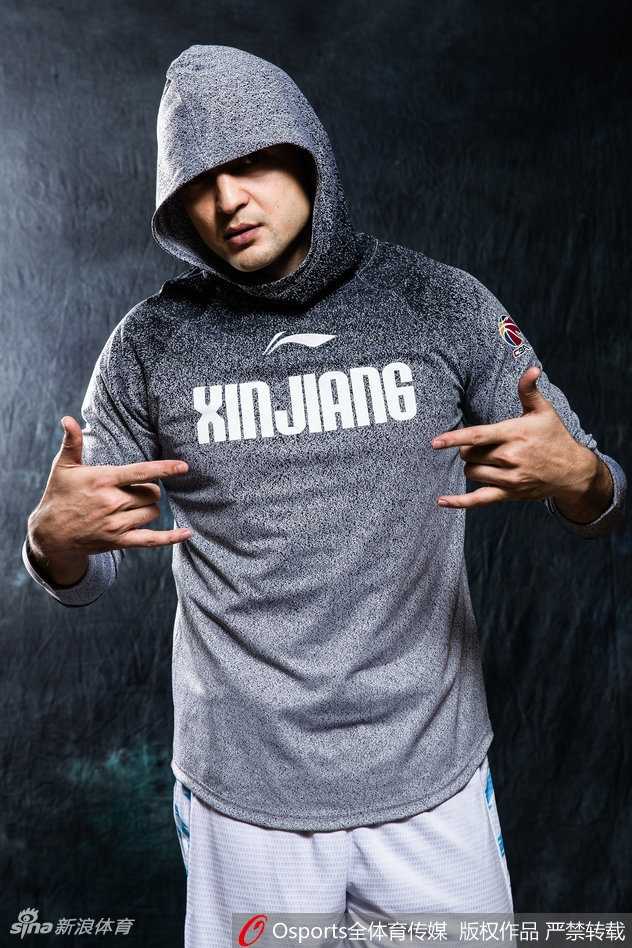 西热力江坐在椅子上身体前倾，双手交叉，身着时尚运动装，表情严肃而富有攻击性，如同场上指挥交通的组织后卫