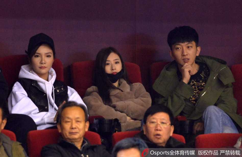 丁彦雨航的女友与睢冉的妻子在喧闹的看台上窃窃私语，脸上带着默契的微笑，仿佛在分享着只有彼此才懂的秘密。