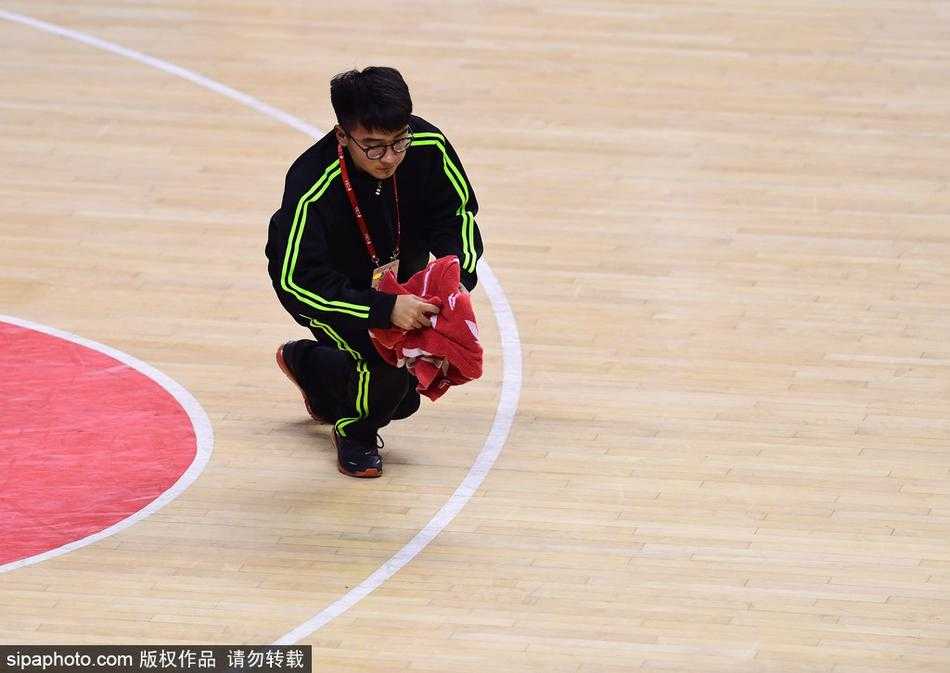 裁判与球员围成一圈争球瞬间，场边穿着橙色马甲的“地板工”手持毛巾安静等待，随时准备履行职责