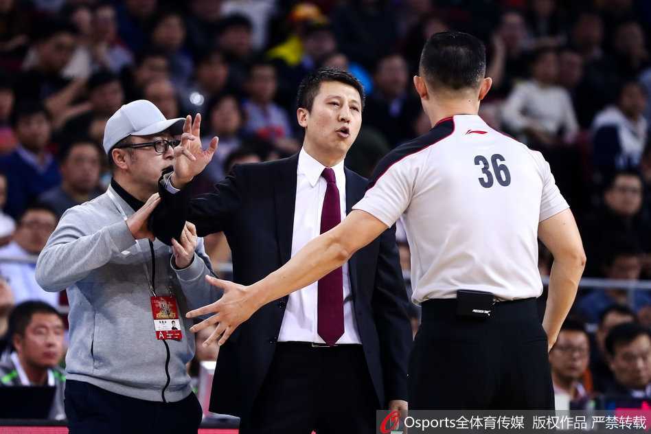 郭士强指向远处的记分牌，仿佛在告诫队员不要忘记这一刻的比分。他的眼神坚毅而有力，即使比赛处于被动，他也从未放弃过对胜利的渴望。辽宁队的蓝色球衣在灯光下格外醒目，映衬着这位东北教头的铁血风骨。