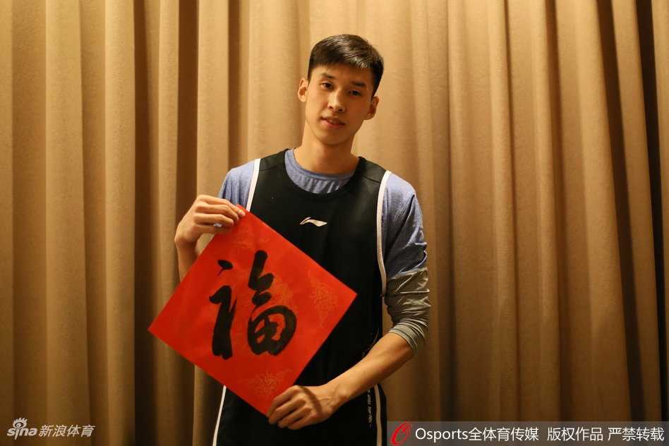 画面中的雷蒙剑眉星目，嘴角微扬，彼时刚成为球队核心的他眼神中既有年轻人的锐气，又带着几分过年的喜气。他手中的红色围巾与背景的节日装饰交相辉映，仿佛在诉说着这个东北大男孩在宁波的拼搏与成长，也代表着球队在新一年里渴望红红火火的愿景。