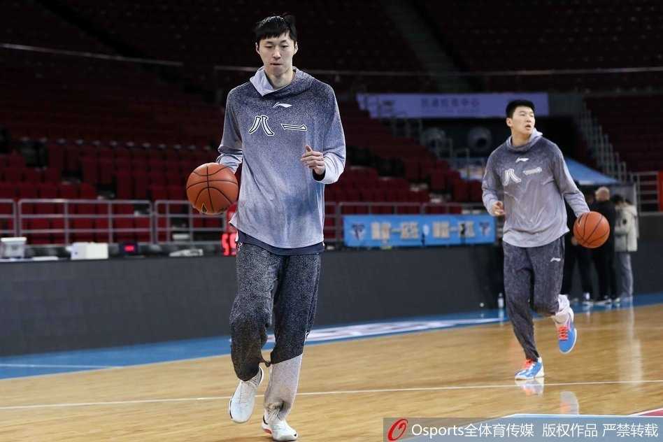 王治郅双手持球置于身前，正面指导一位八一队员，两人目光交汇，正在进行着关于战术跑位的深度交流，空气中弥漫着专注与严肃的气息。