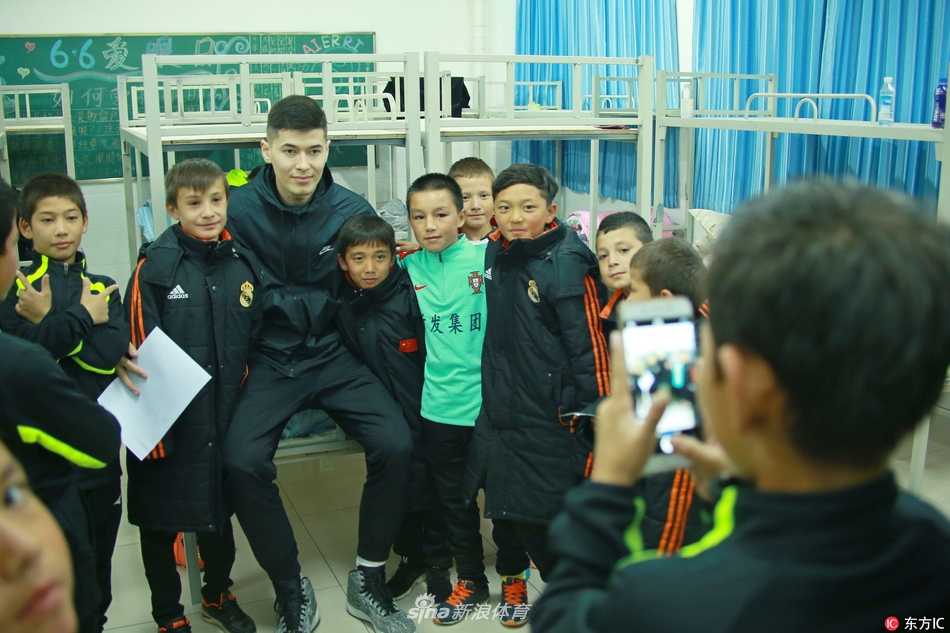 新疆男篮球星阿不都-沙拉木面带微笑，亲切地搂着几位穿着足球装备的小球员肩膀，眼神中满是鼓励与期许。
