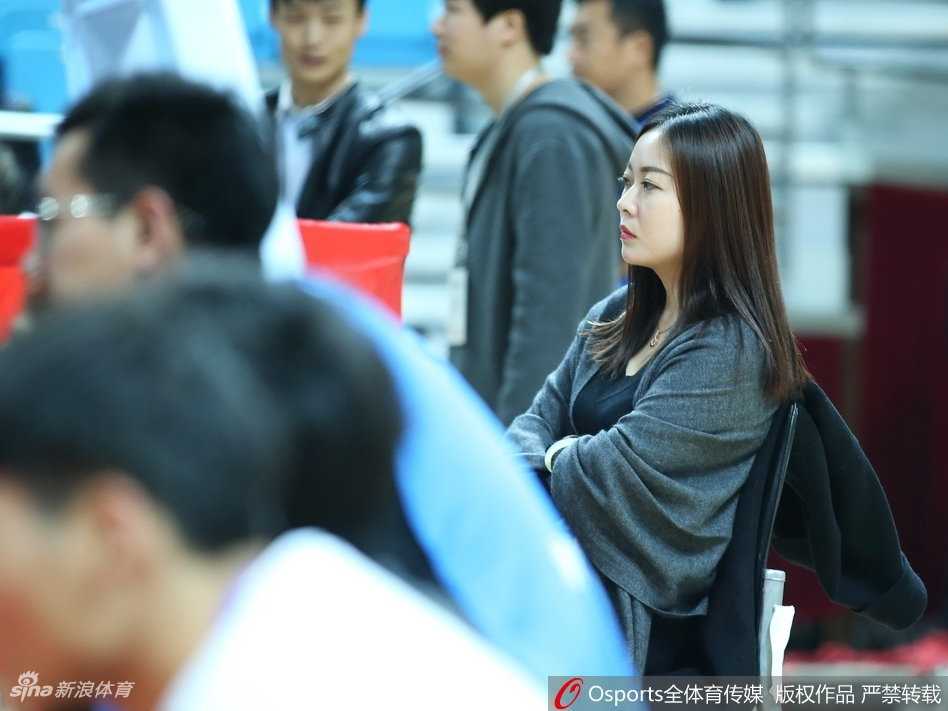 一位笑容灿烂的女球迷在人群中格外醒目，她身着休闲冬装，双手轻抚脸颊，青春的气息扑面而来