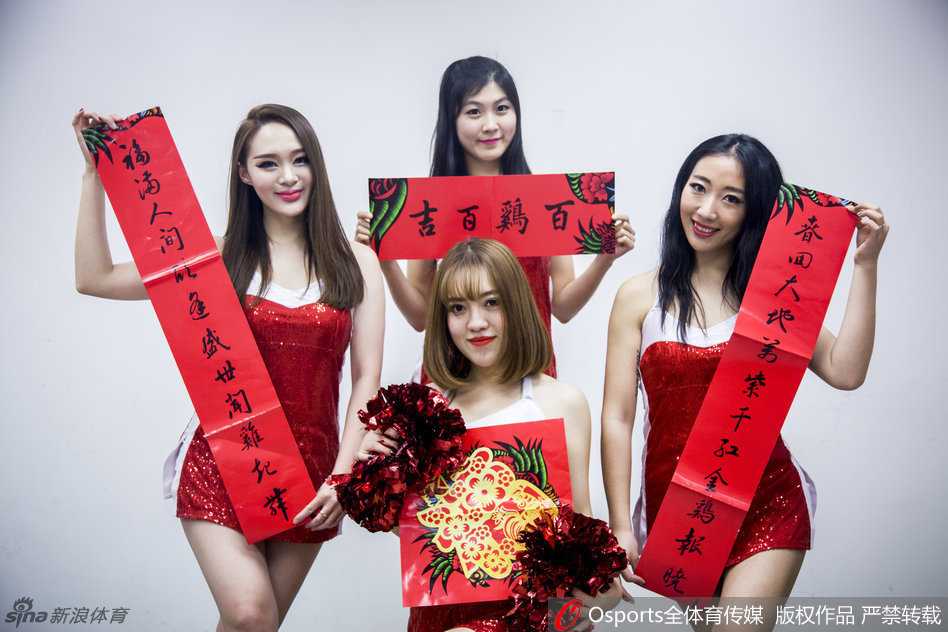 一名宝贝手持充满设计感的镂空扇子半遮面，眼神灵动俏皮，红色的新春装饰与球馆的蓝色座椅形成鲜明对比，洋溢着节日氛围