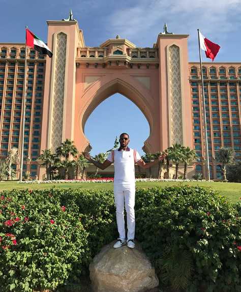 亚当斯身穿简约的白色T恤，在迪拜的建筑背景下单手插兜，表情自信而放松，宛如时尚大片。