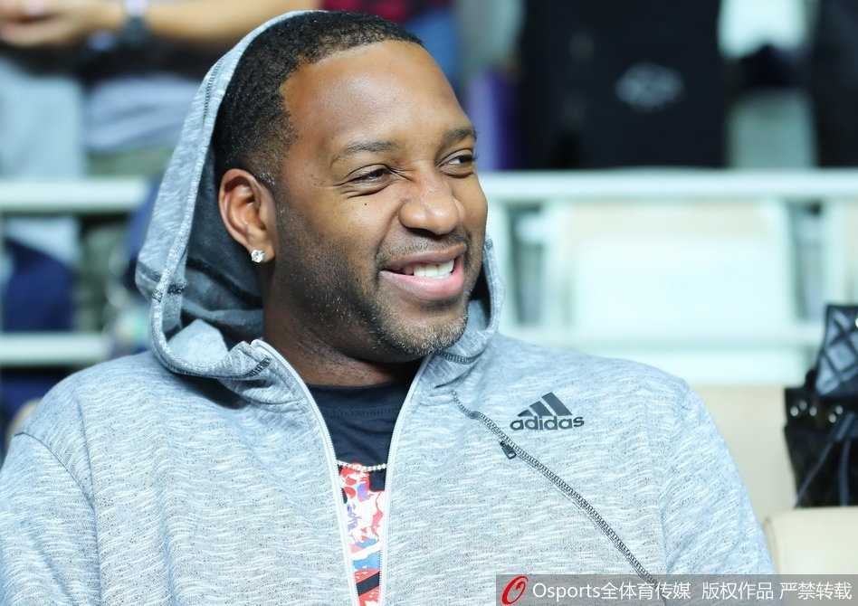 麦蒂神情专注地看着场上的激烈对抗，双手轻轻合拢放在腿上，眼神随着篮球的轨迹移动，完全沉浸在这场高水平的对决之中。