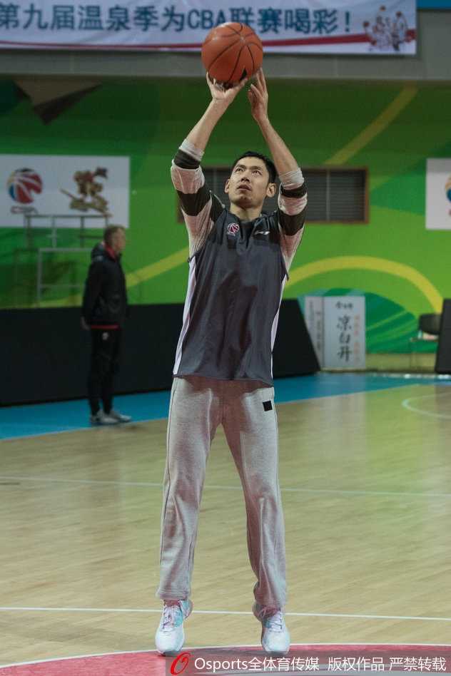 体能教练受到丁彦雨航的感染，正聚精会神地从篮架后方尝试高难度投篮，队友们站在一旁准备抢篮板，脸上洋溢着轻松的笑容。