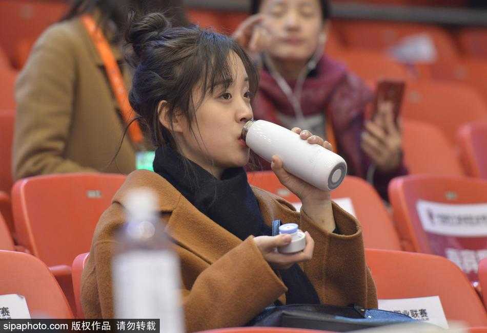 一位戴着眼镜的知性美女球迷，在人群中露出甜美的微笑，她或许是被比赛的某个精彩瞬间所打动，笑容里满是参与其中的快乐。