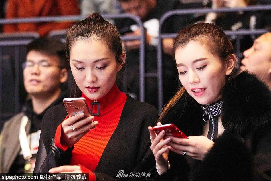 看台一角，小丁女友与身旁的友人轻声交谈，脸上带着放松的神情，身后的背景板印着全明星赛的标识，她手中的手机或许正在记录着这一刻，期待着将男友的赛场英姿永久珍藏。