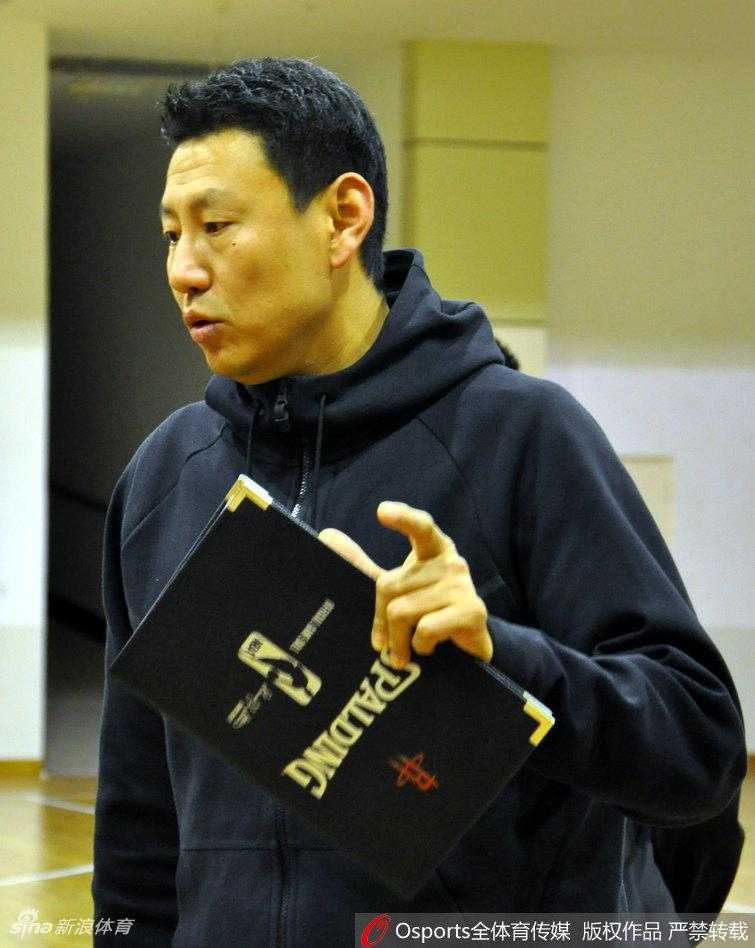 主教练李楠指导双手叉腰站在场边，目光如炬地注视着场内训练，神情专注，随时准备叫停纠正球员的技术动作。